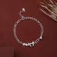 Silver chain bracelet with heart and elephant charms on a brown background