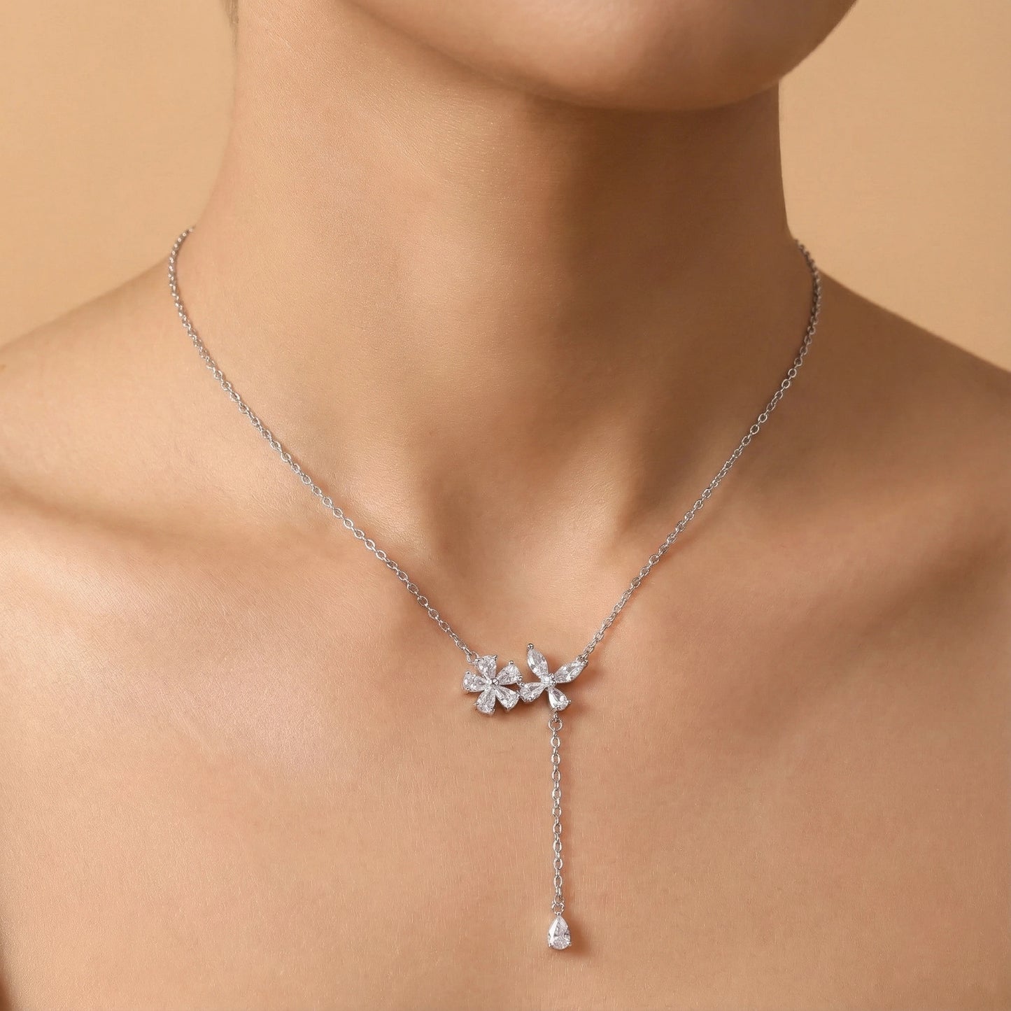 Silver necklace with floral pendant on a person against a beige background