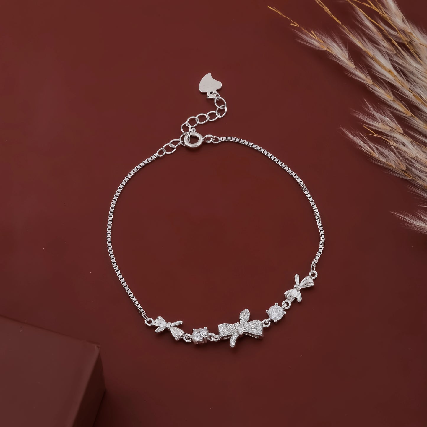 Silver bracelet with floral and bow charms on a brown background