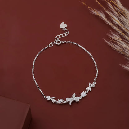 Silver bracelet with floral and bow charms on a brown background