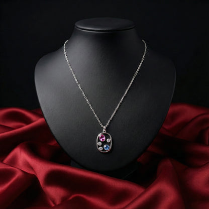 Silver necklace with a multicolored pendant on a black mannequin bust against a red fabric background