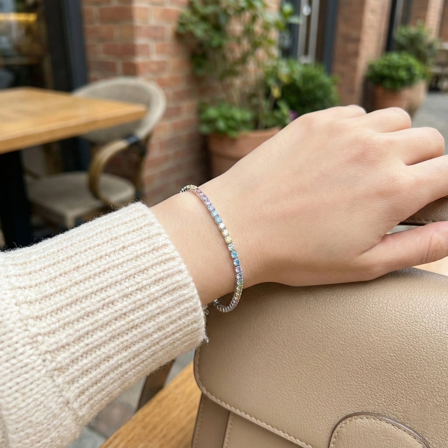 Hand wearing a colorful beaded bracelet with a blurred outdoor cafe background