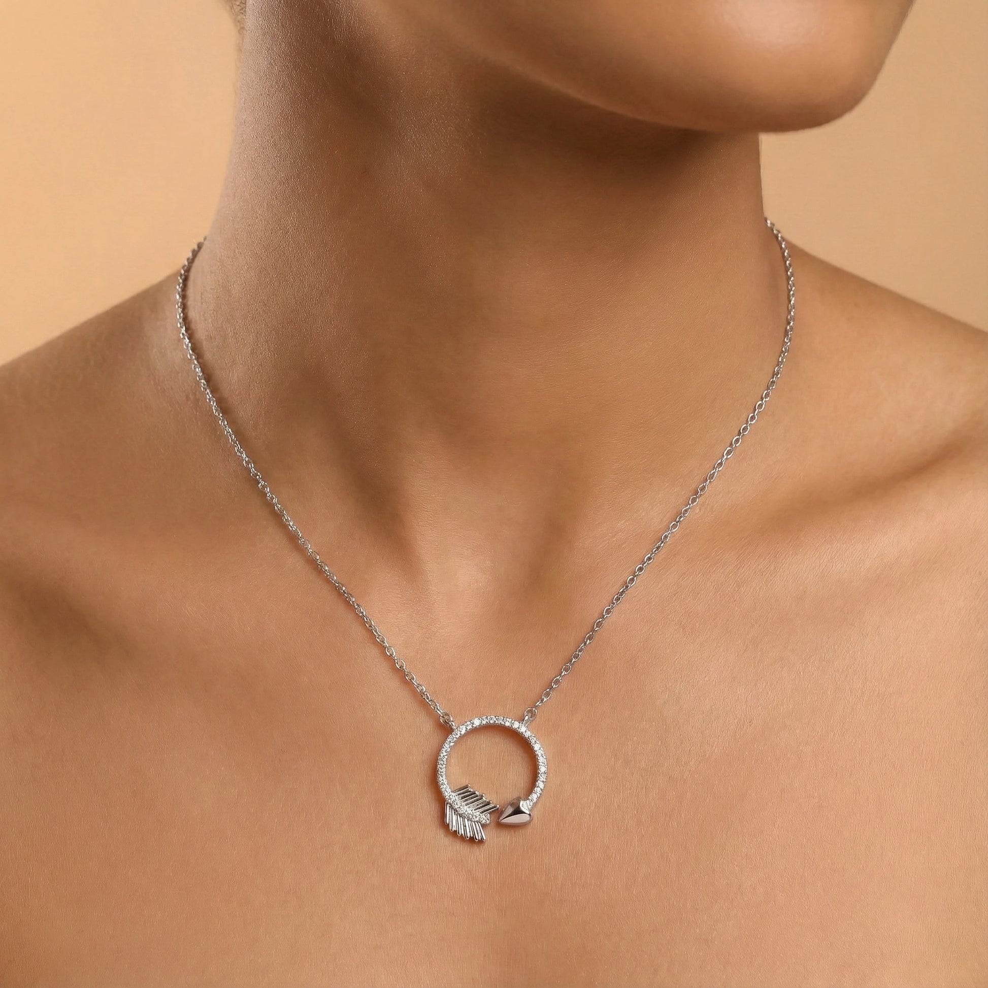 Silver necklace with a circular pendant on a person against a beige background