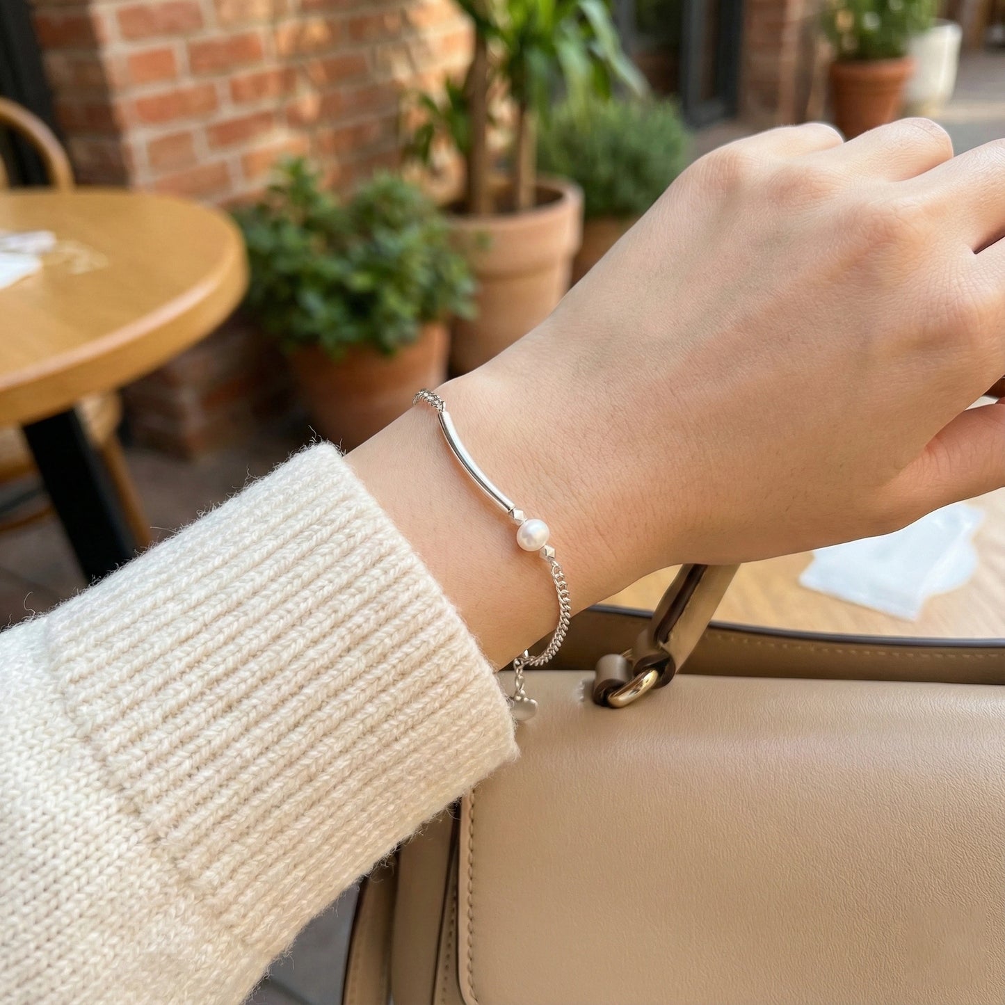 Hand wearing a silver bracelet with a pearl on a blurred cafe background