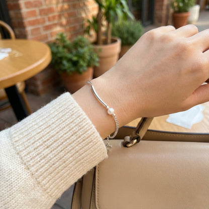 Hand wearing a silver bracelet with a pearl on a blurred cafe background