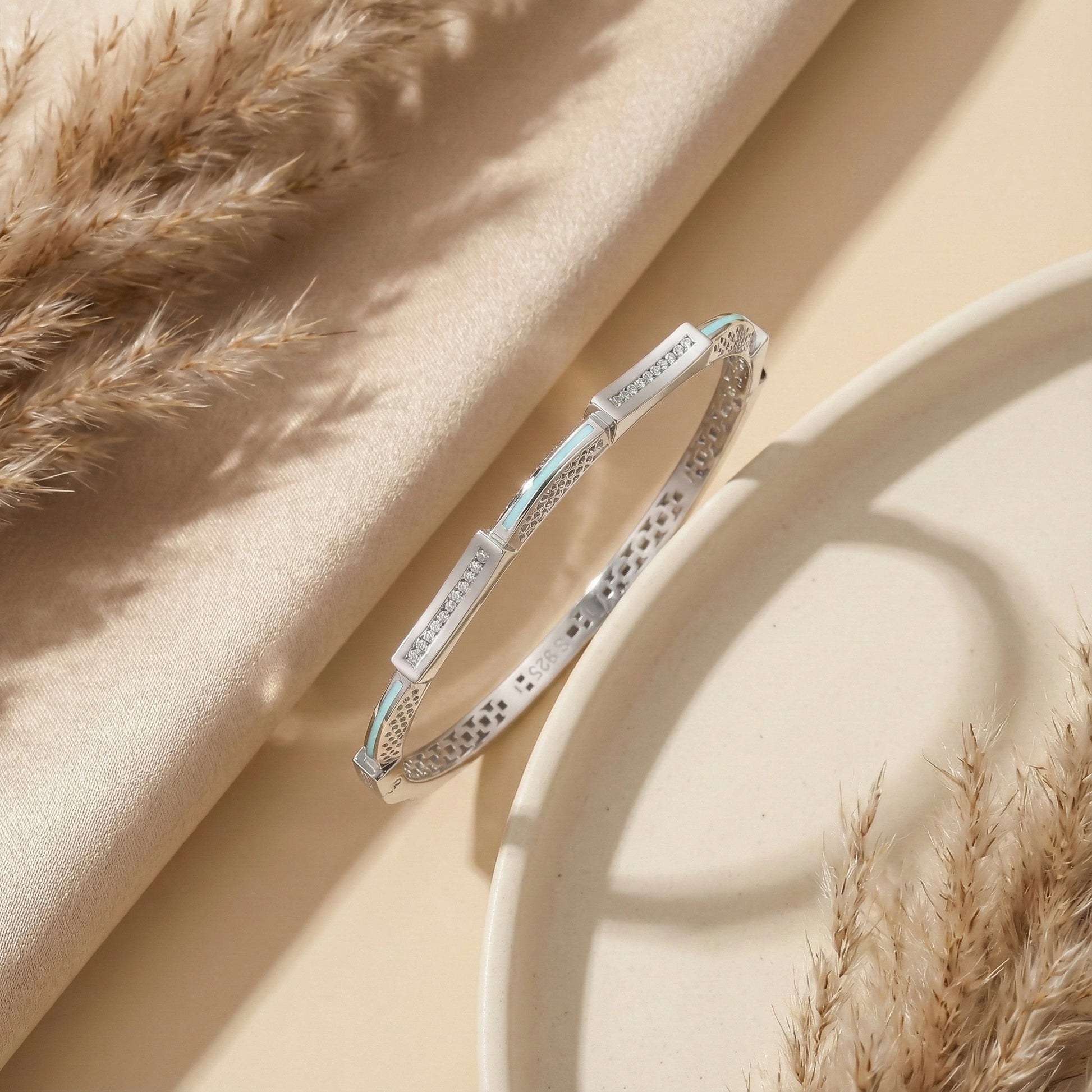 Silver bracelet with blue accents on a beige fabric background with dried grasses.