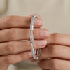 Silver bracelet with blue accents held between fingers against a neutral background