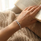 Hand wearing a bracelet holding an open book on a textured surface