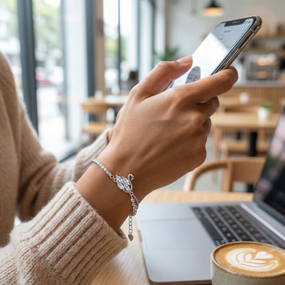 Person using a smartphone in a cafe with a laptop and coffee cup on the table.