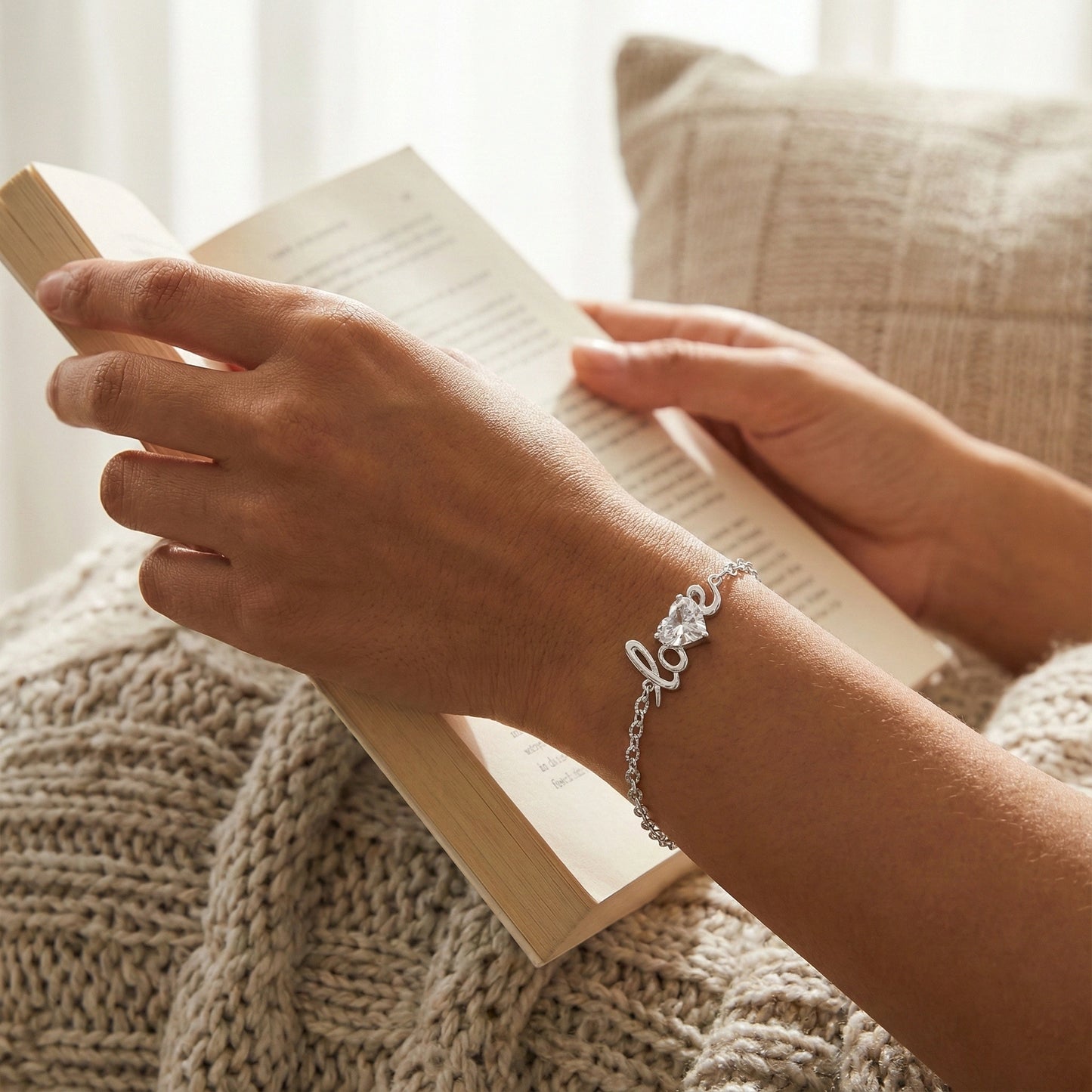 Person holding a book with a bracelet on wrist, sitting on a textured surface.