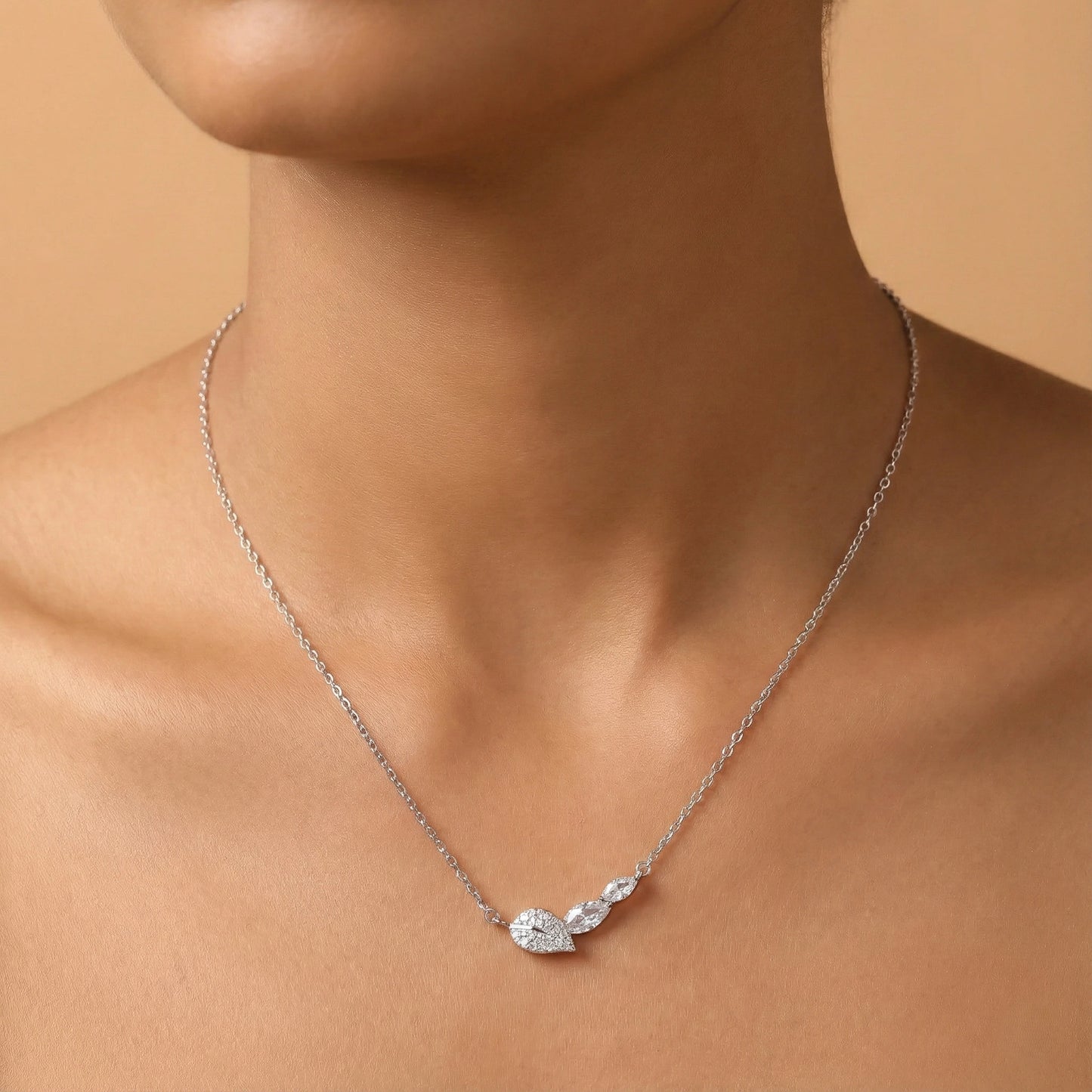 Silver necklace with a leaf-shaped pendant on a person against a beige background