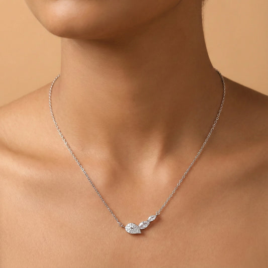 Silver necklace with a leaf-shaped pendant on a person against a beige background