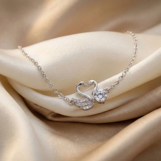 Silver swan necklace with a heart-shaped pendant on beige fabric
