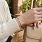 Person wearing a silver bracelet with butterfly charms, holding a beige handbag outdoors.