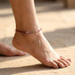 Ankle with a beaded anklet on a sandy background