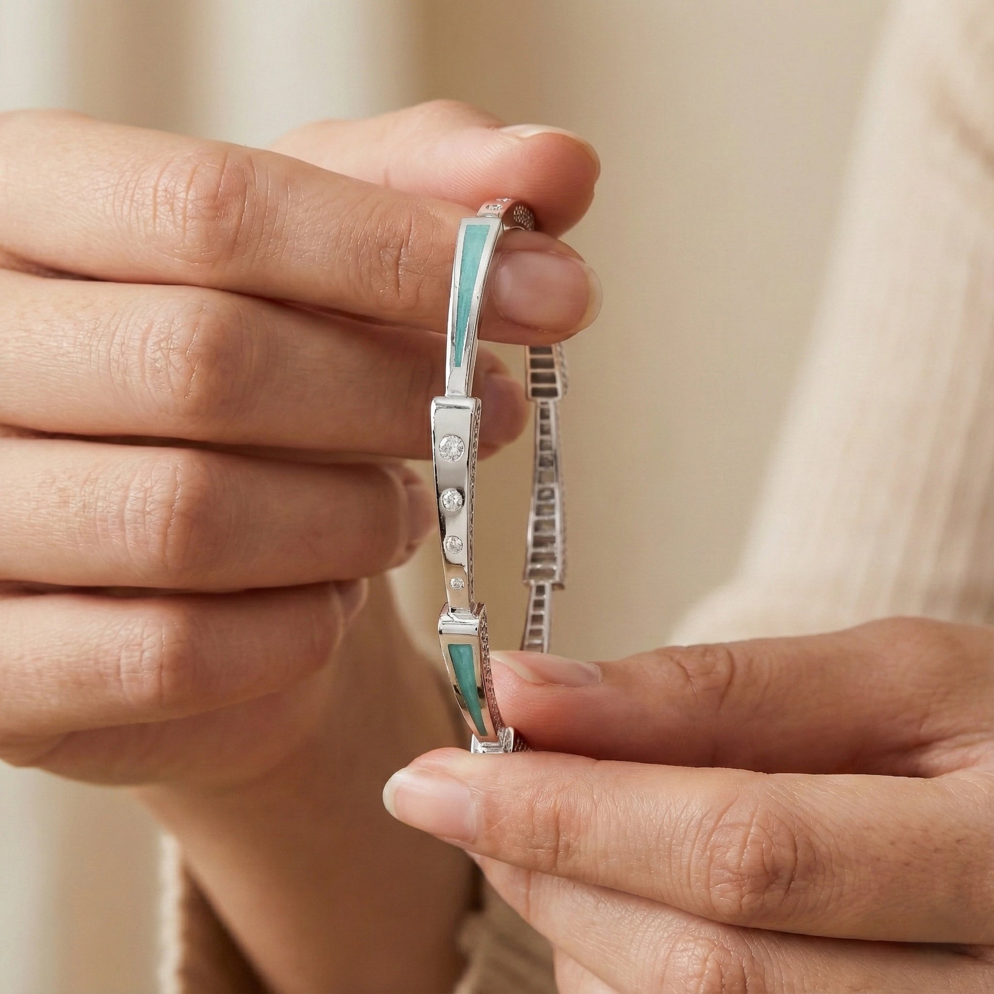 Close-up of hands holding a silver bracelet with turquoise accents against a neutral background