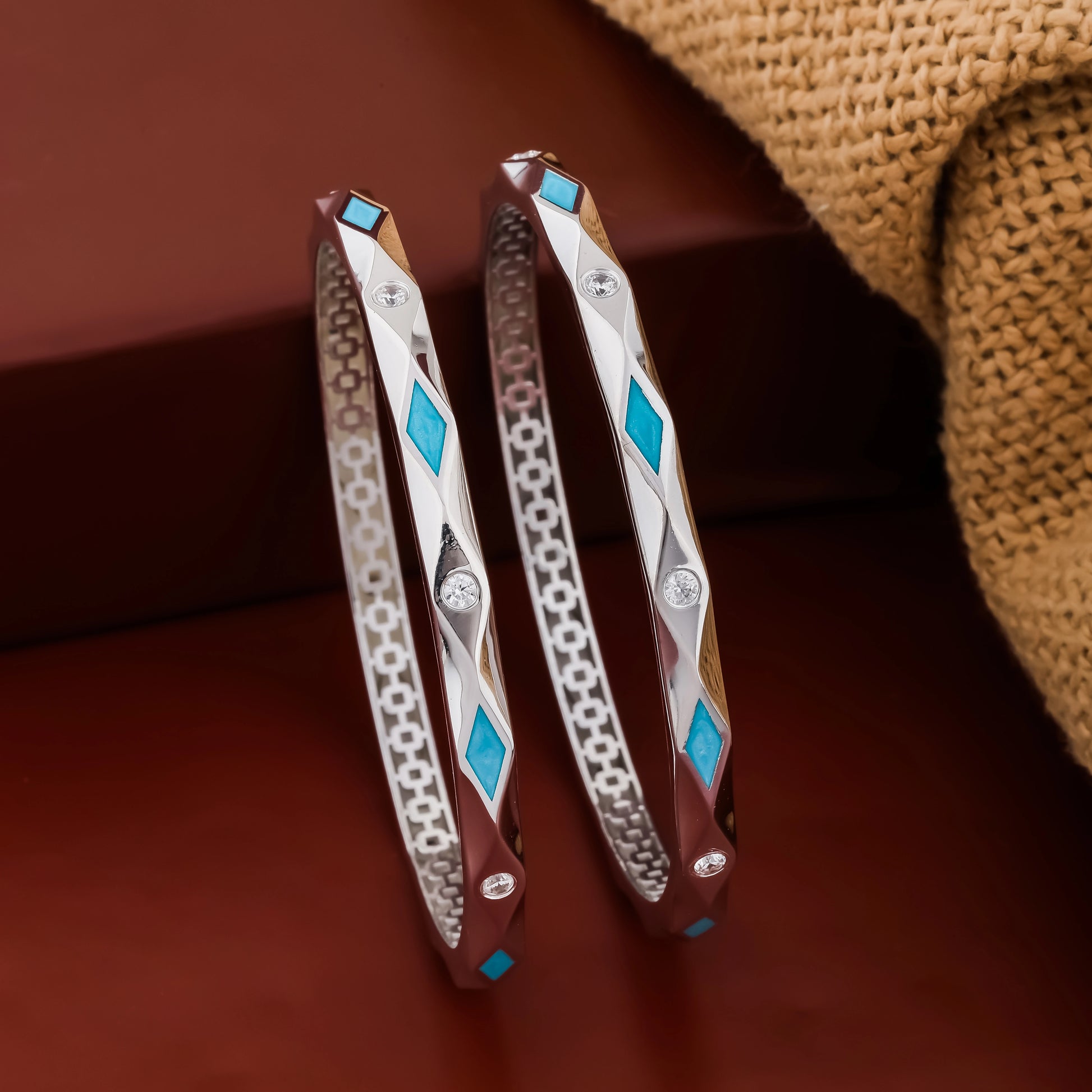 Two silver bangles with blue gemstones on a brown surface