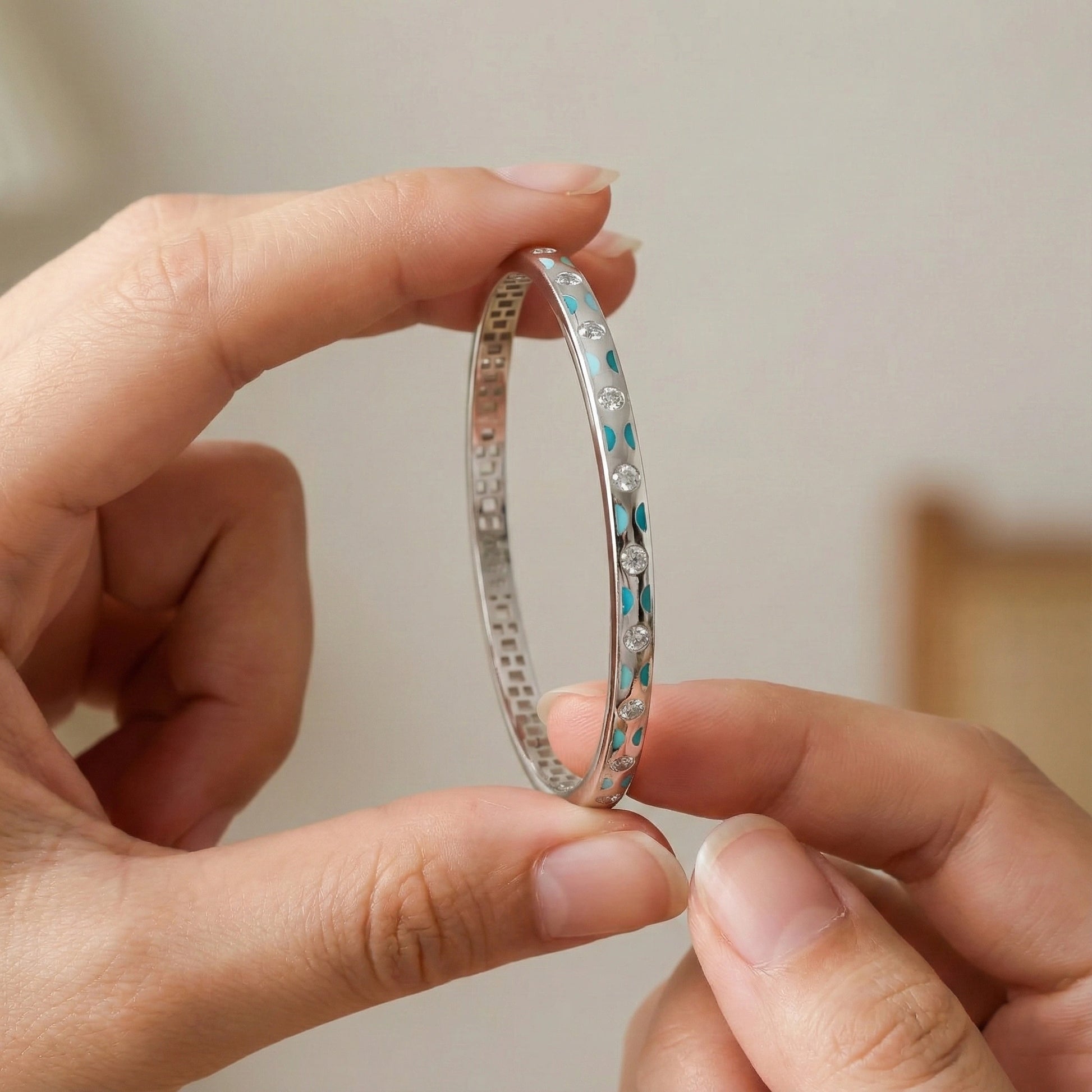 Silver bangle with blue stones held between two fingers against a neutral background