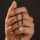 Hand holding a black beaded necklace with a silver clasp against a dark background