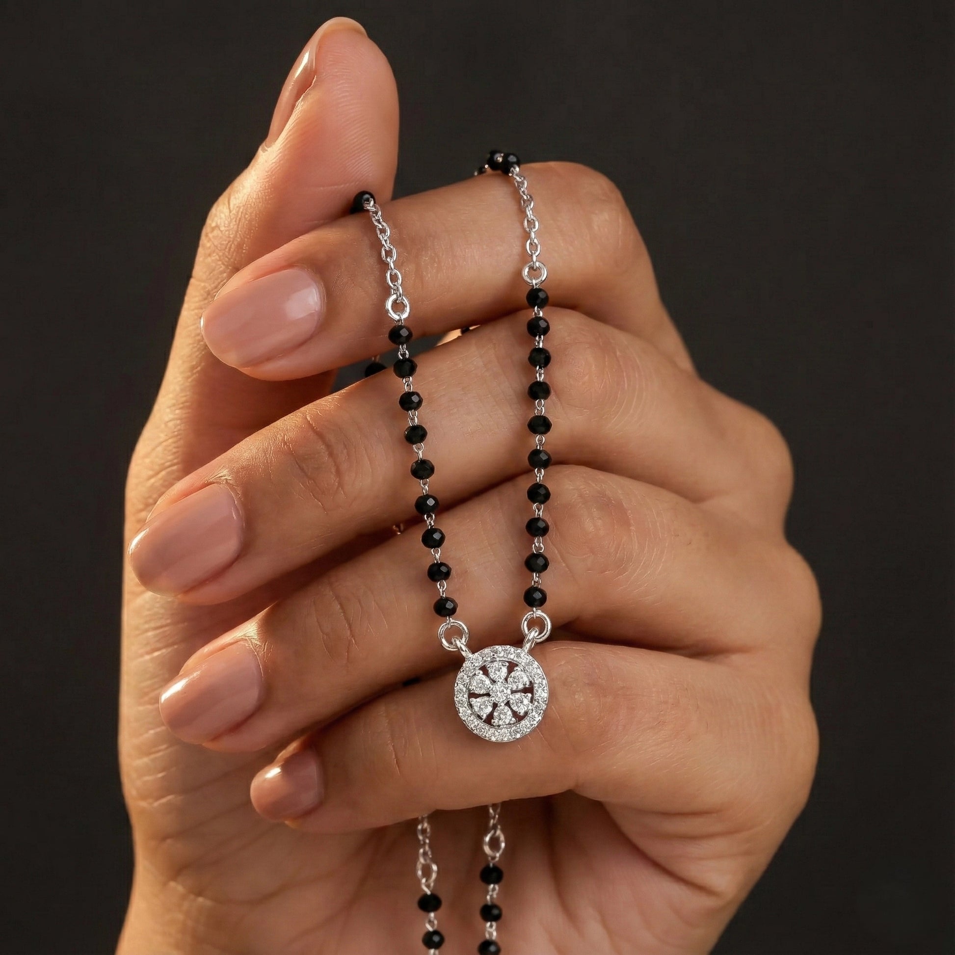 Hand holding a black beaded necklace with a silver clasp against a dark background