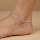 Silver anklet on a foot against a beige background