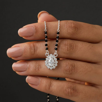 Hand holding a necklace with a diamond pendant against a dark background