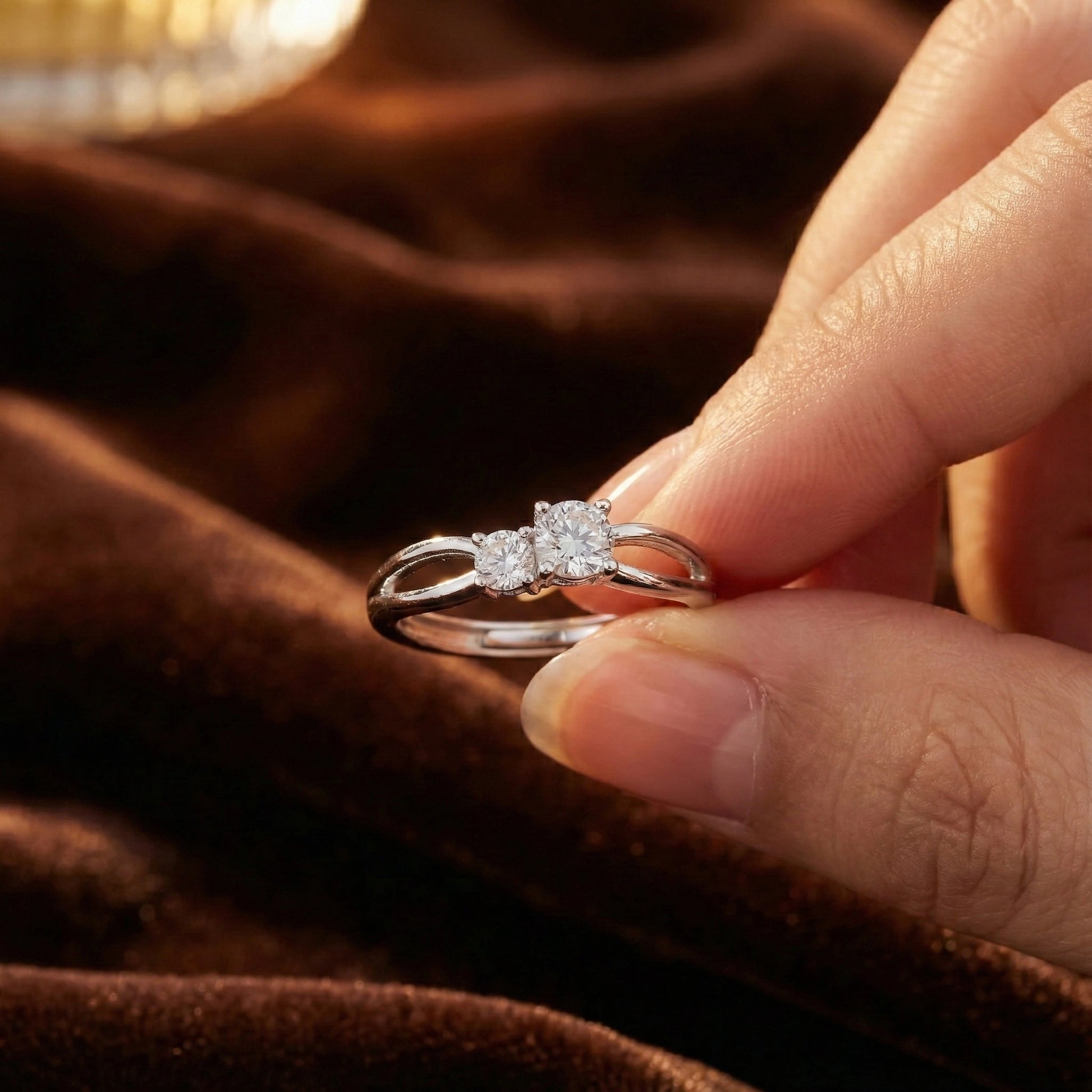 Silver ring with a diamond held between fingers on a brown fabric background