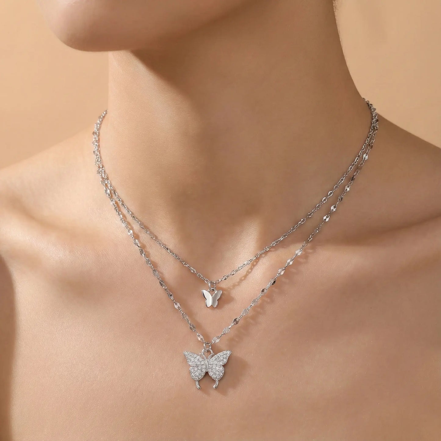 Silver butterfly necklace on a person against a beige background
