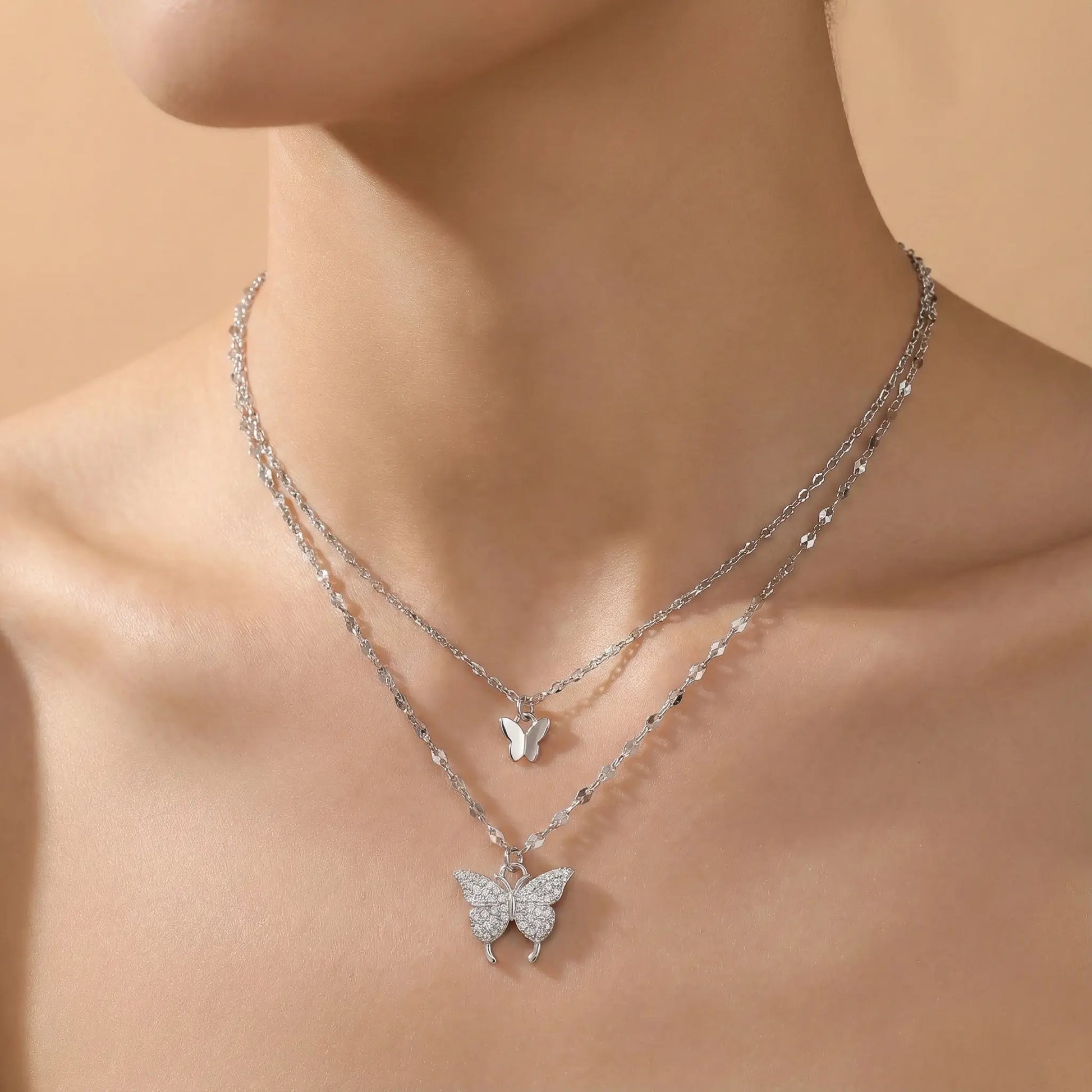 Silver butterfly necklace on a person against a beige background