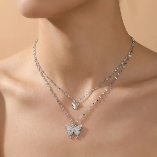 Silver butterfly necklace on a person against a beige background