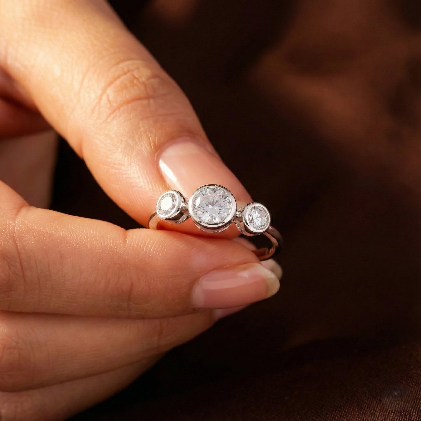Silver ring with three round diamonds on a person's finger against a dark background