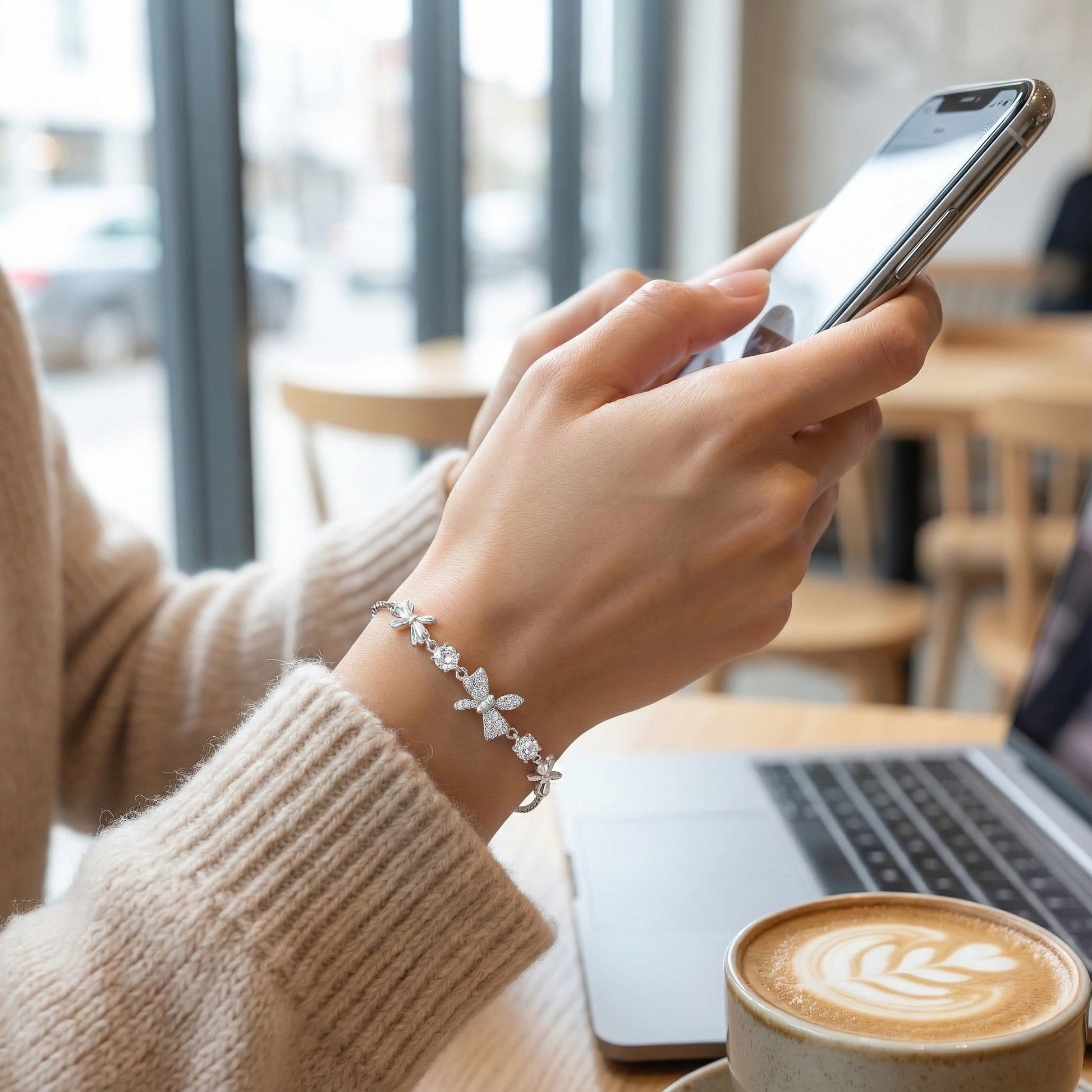 Person using a smartphone with a cup of coffee and laptop on a table in a cafe.