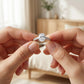 Close-up of hands holding a diamond ring with a blurred indoor background