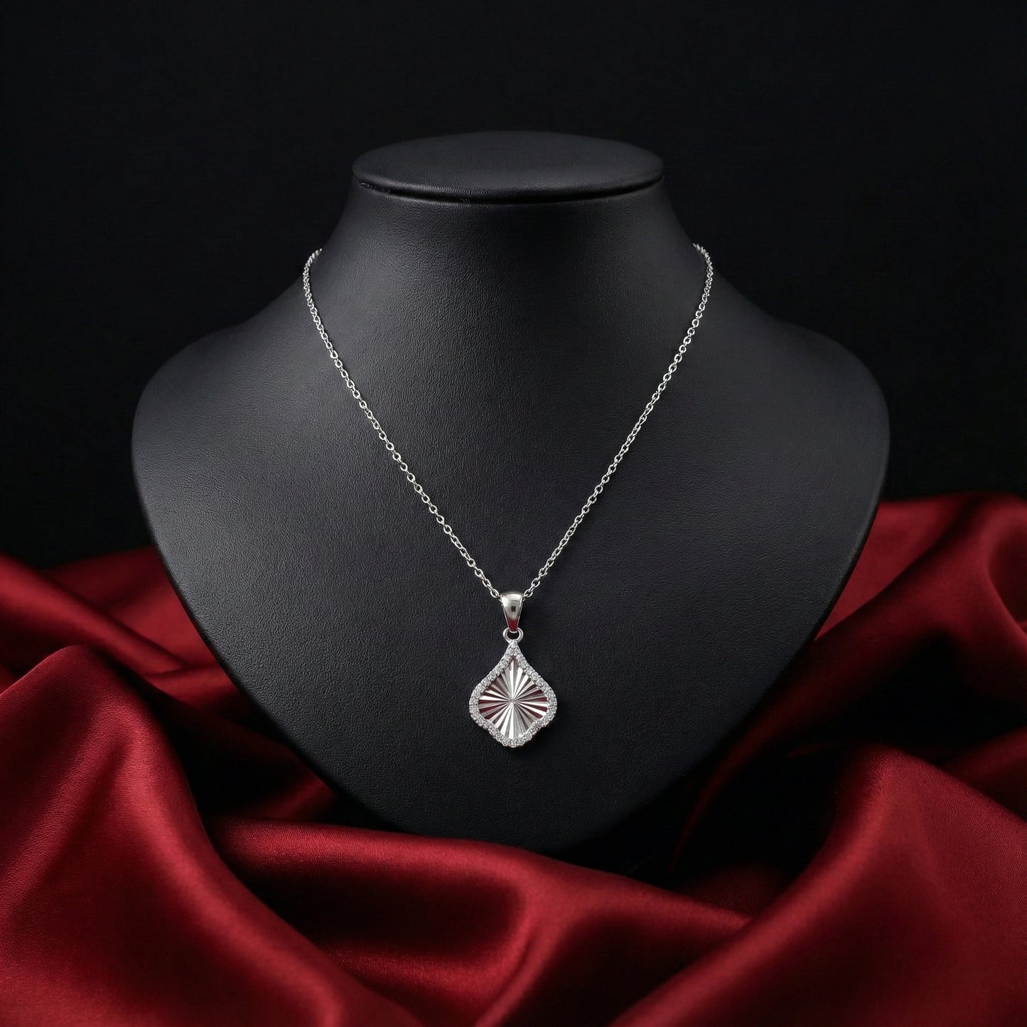 Silver necklace with a pendant on a black mannequin bust against a red fabric background