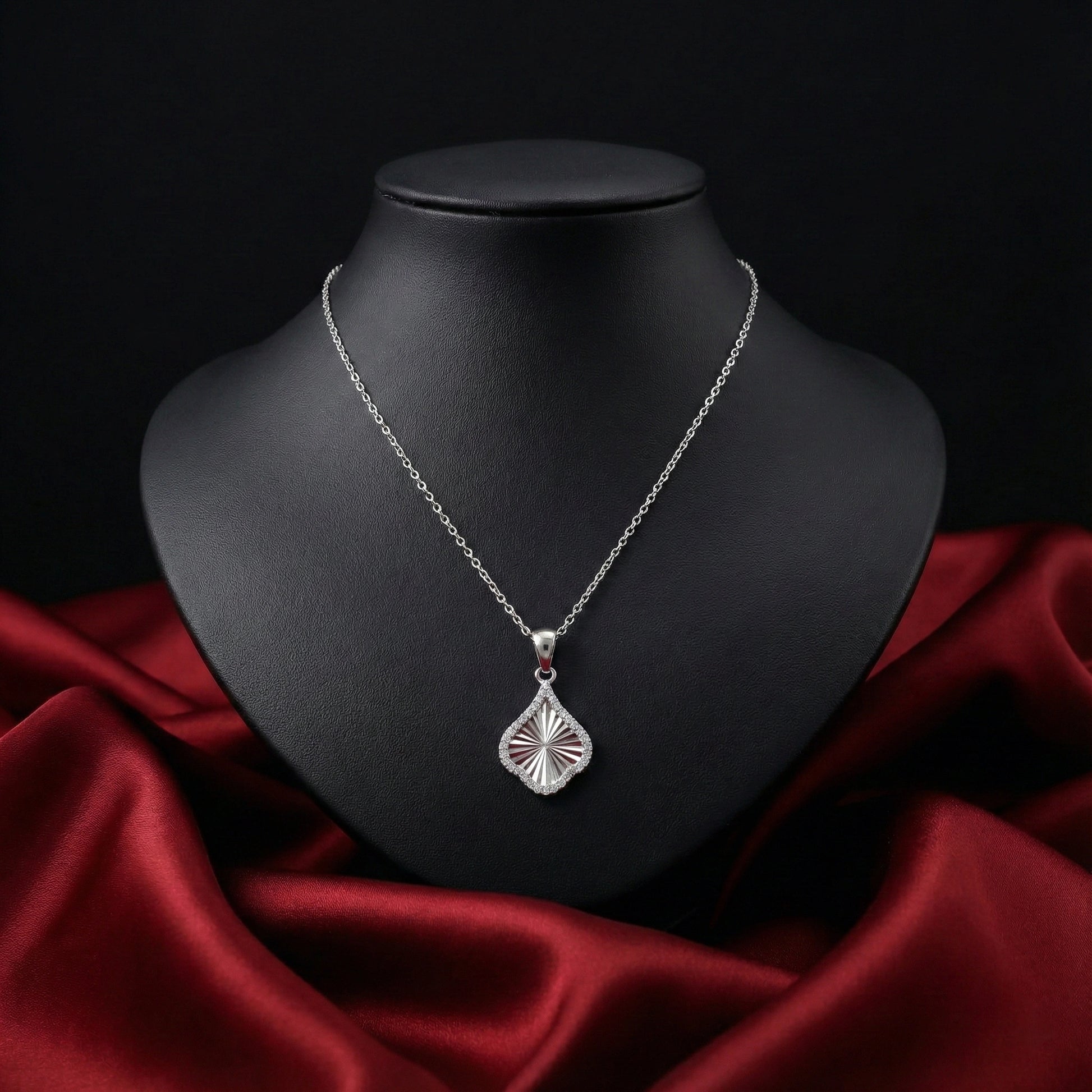 Silver necklace with a pendant on a black mannequin bust against a red fabric background