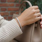 Hand holding a beige handbag with a blurred brick wall background
