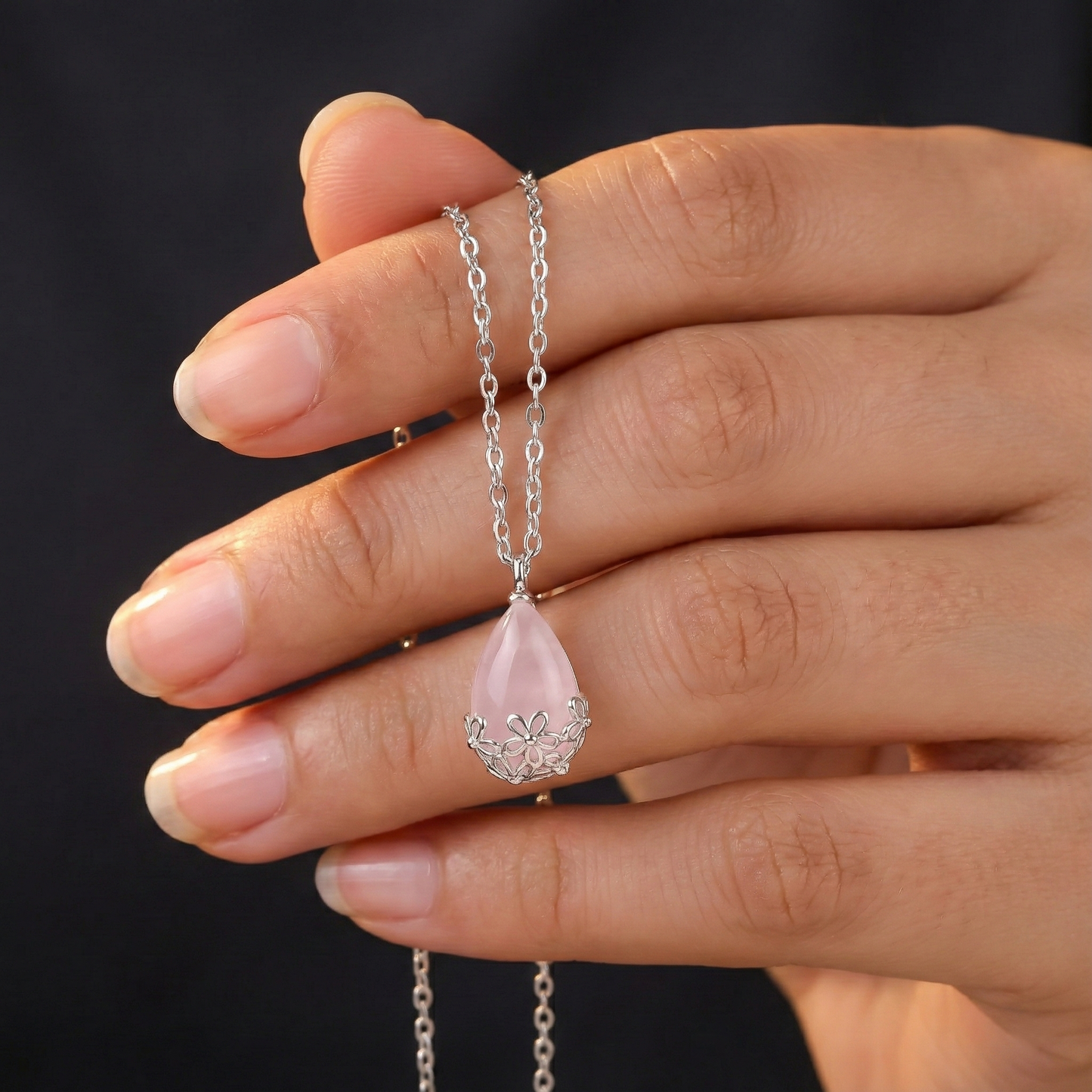 Hand holding a delicate necklace with a pink teardrop pendant against a dark background