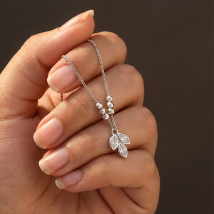 Hand holding a silver necklace with a leaf pendant against a brown background