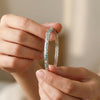 Close-up of hands holding a silver bracelet with small stones against a neutral background