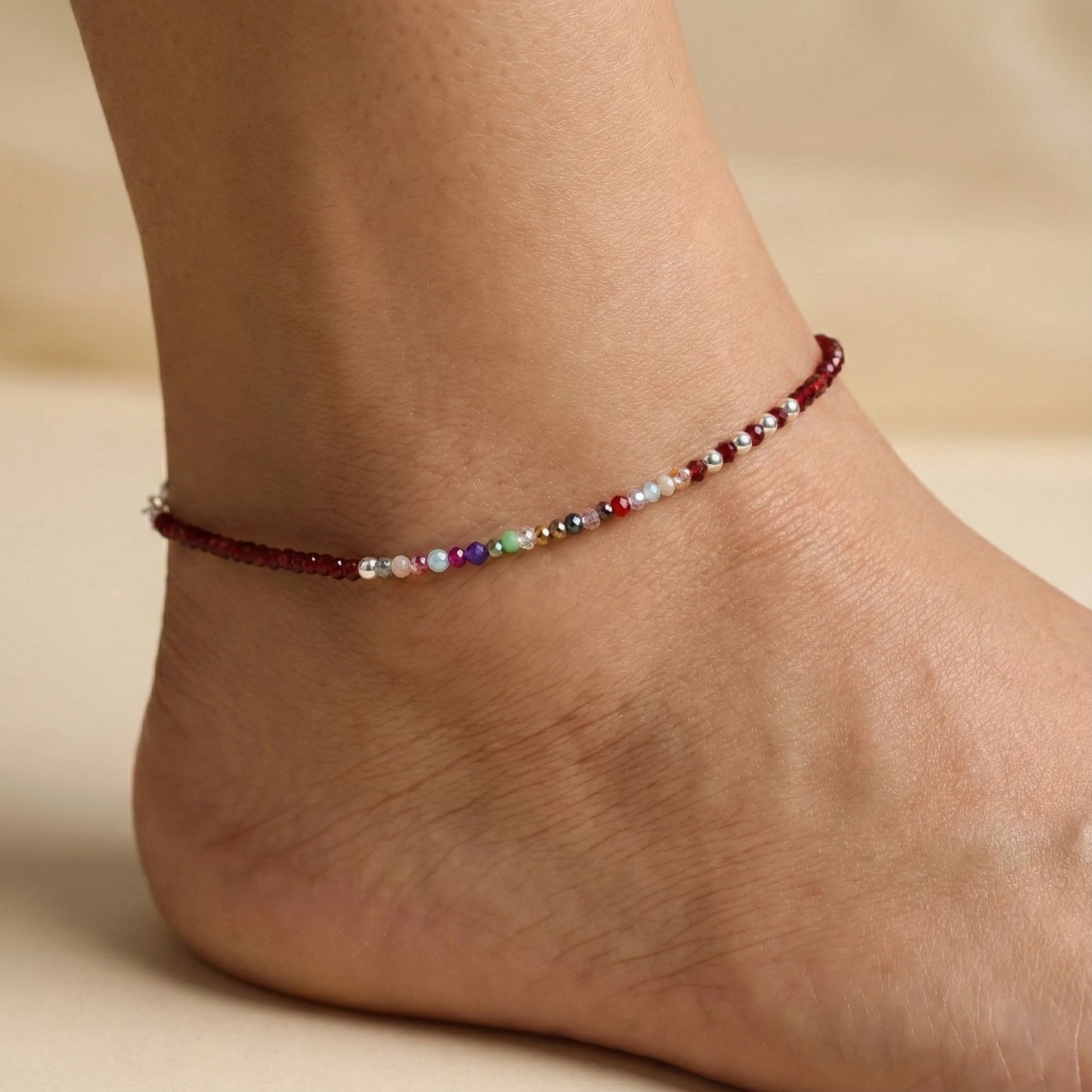 Multicolored beaded anklet on a person's ankle against a neutral background