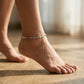 Close-up of a foot wearing a colorful anklet on a wooden floor.