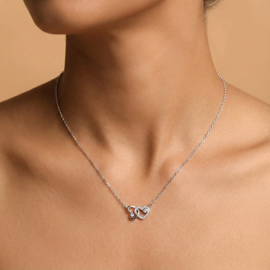 Silver necklace with a heart-shaped pendant on a person against a beige background