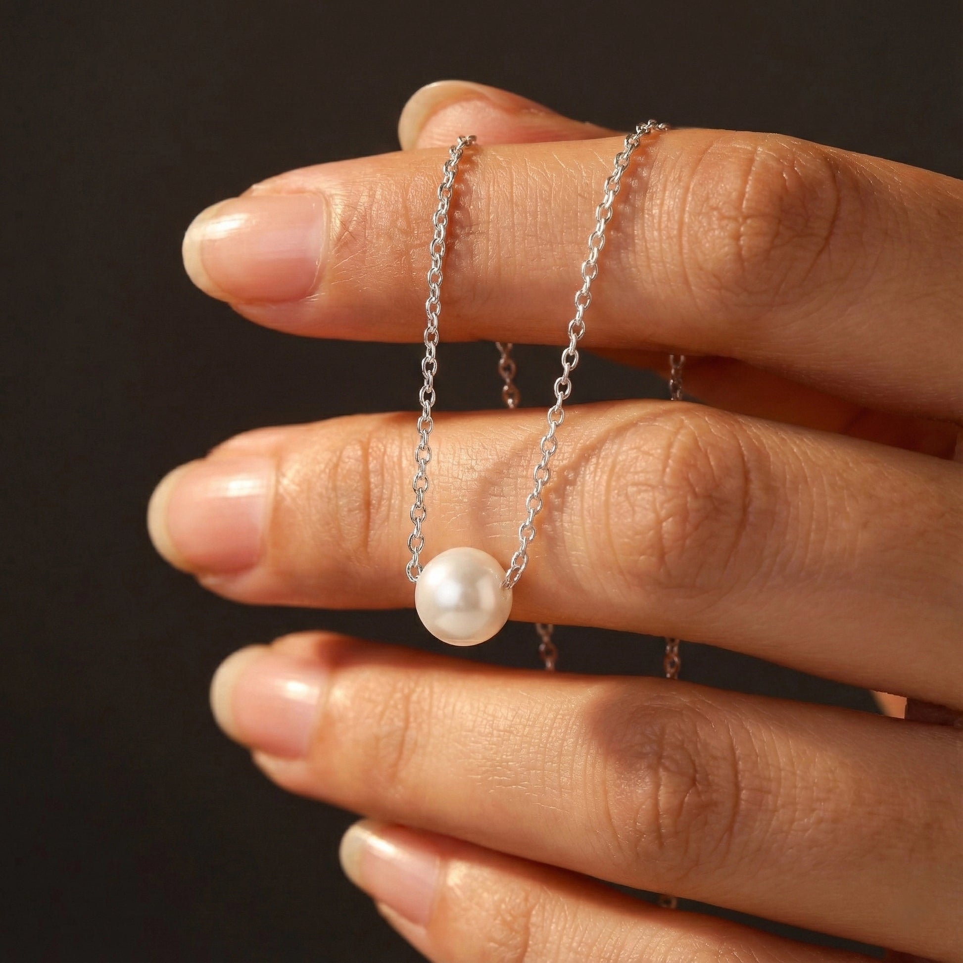 Hand holding a pearl necklace against a dark background