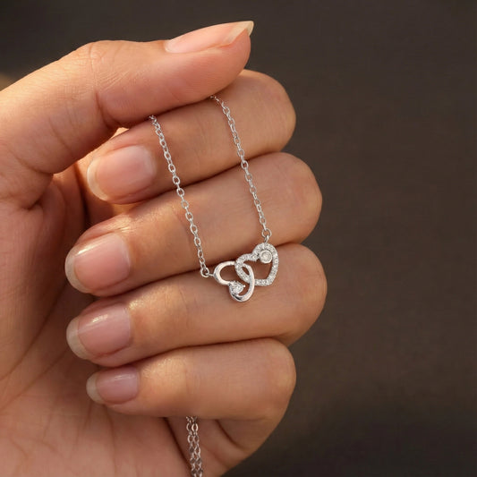 Silver necklace with a heart pendant held by a hand against a brown background