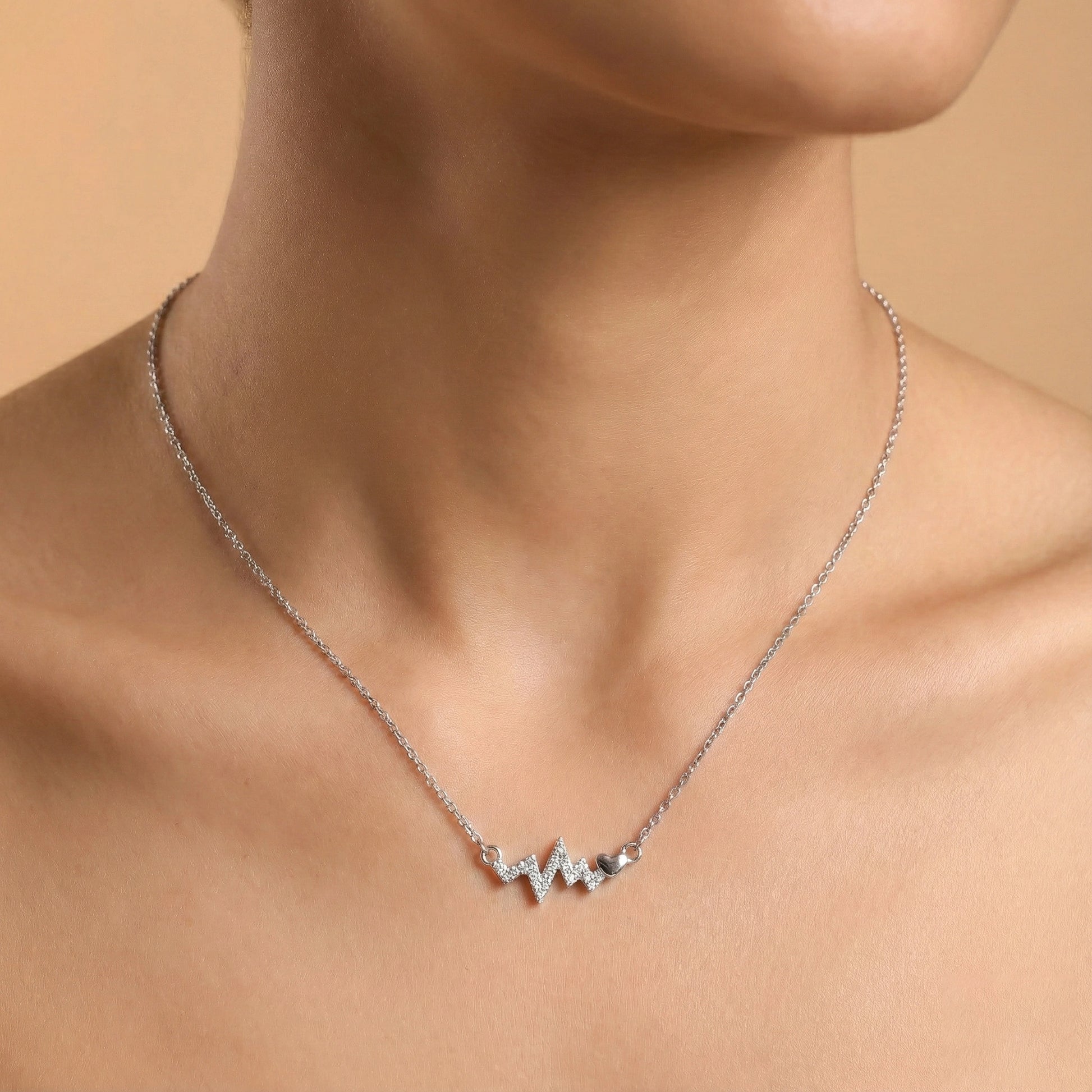 Silver necklace with a unique design on a person's neck against a beige background