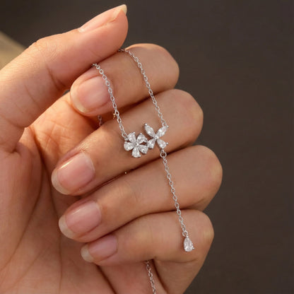 Silver necklace with a floral pendant held in a hand against a brown background