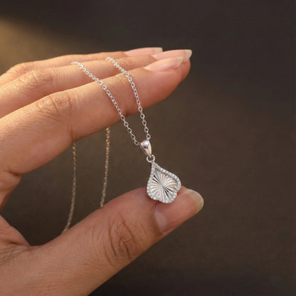 Silver necklace with a pendant held by a hand against a dark background