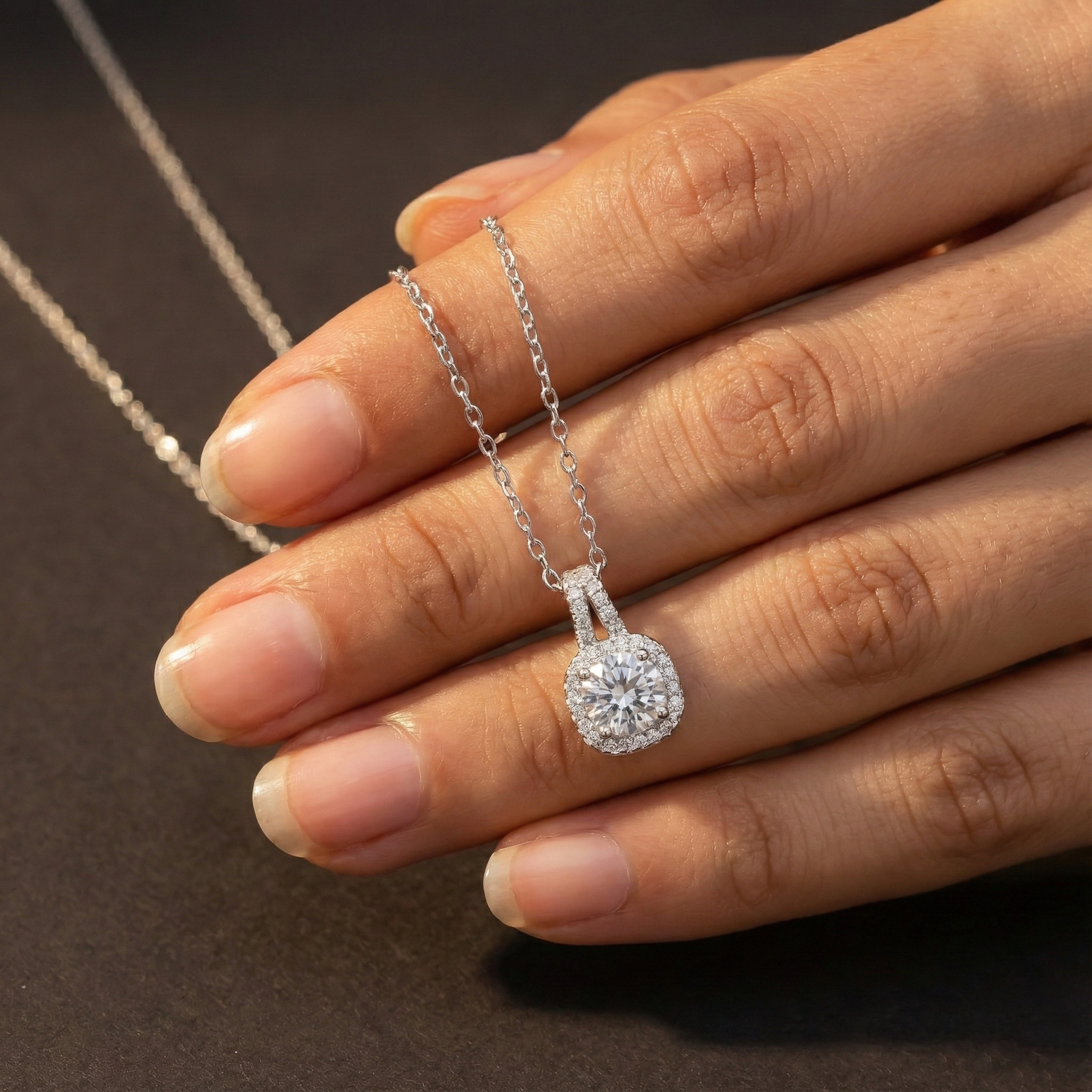 Diamond necklace held by a hand against a dark background