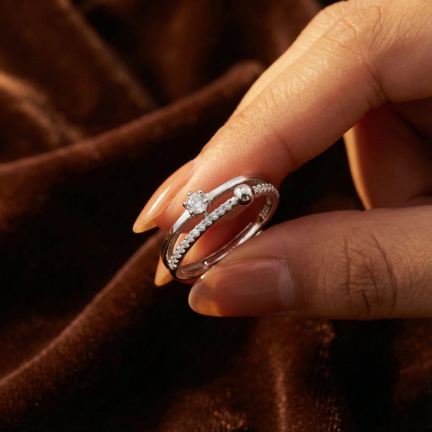 Close-up of a hand wearing two diamond rings on a brown fabric background
