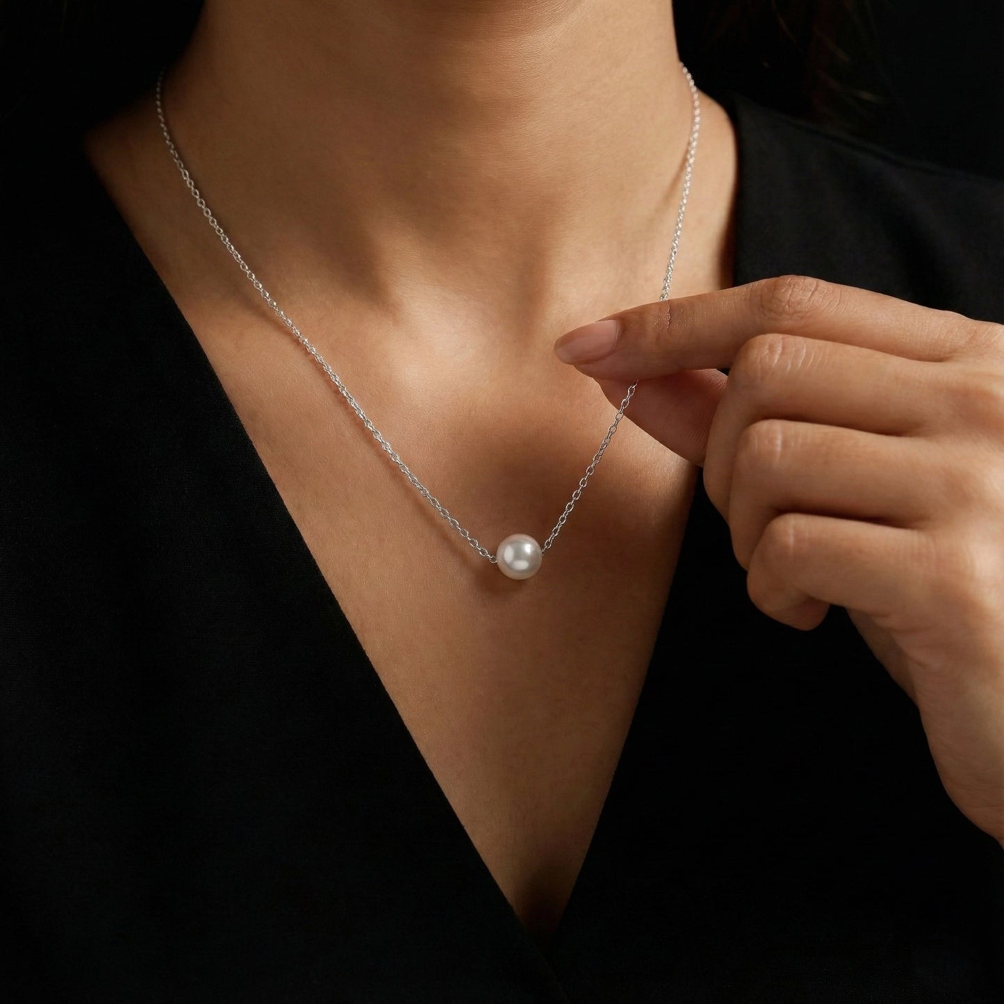 Person wearing a pearl necklace with a hand adjusting it against a dark background
